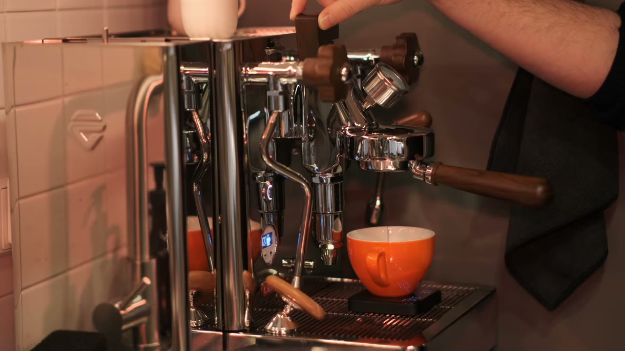 My hand moving the wooden paddle on the Lelit Bianca during a shot into an orange cup
